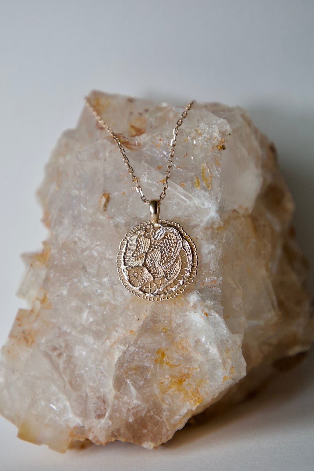 Collier Grâce en vermeil doré à l'or 18 carats, avec médaille ronde aux motifs de dentelle ajourée, posé sur une pierre naturelle beige.